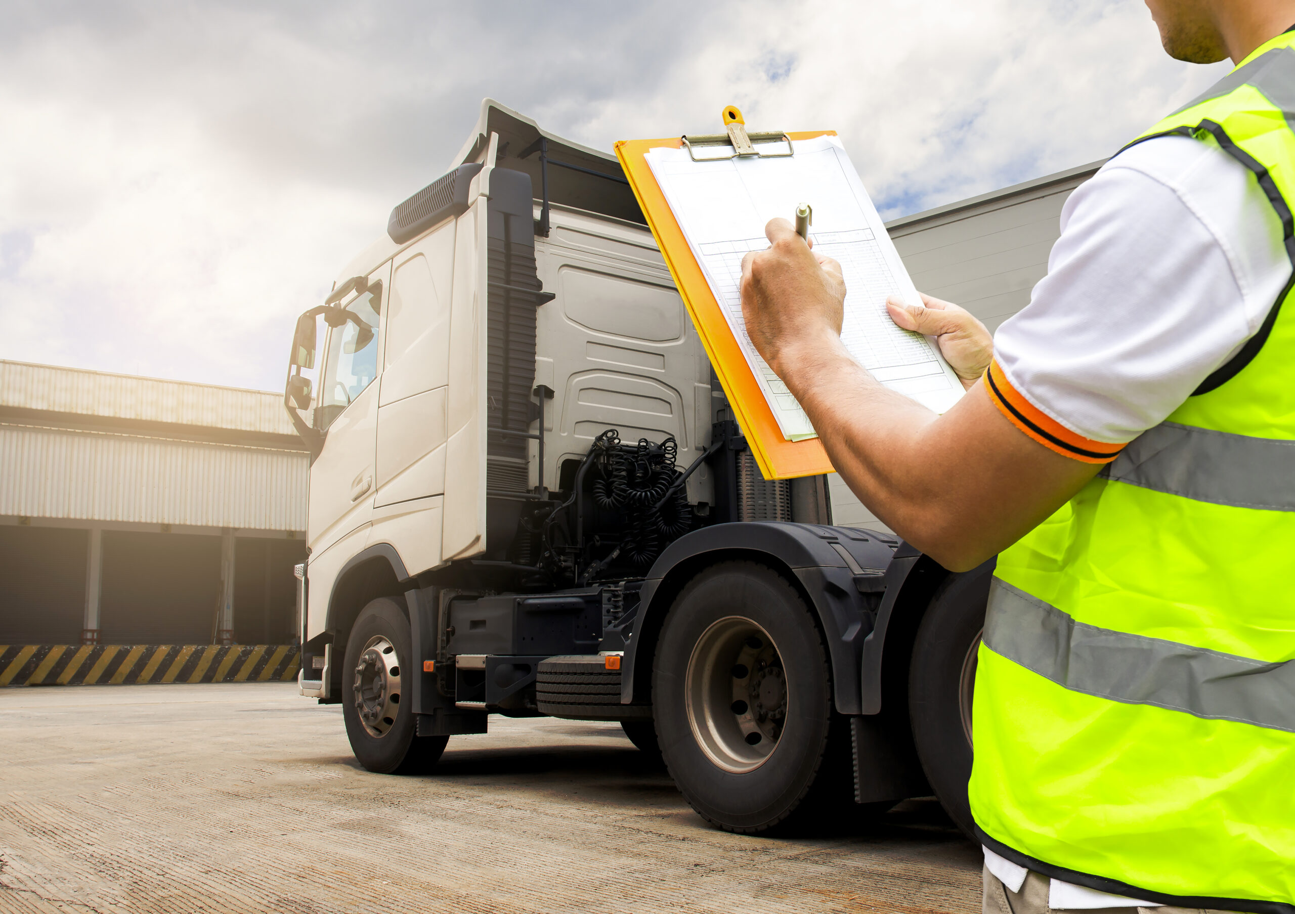 Truck driver hand holding clipboard inspecting safety check maintenance program of a semi truck.